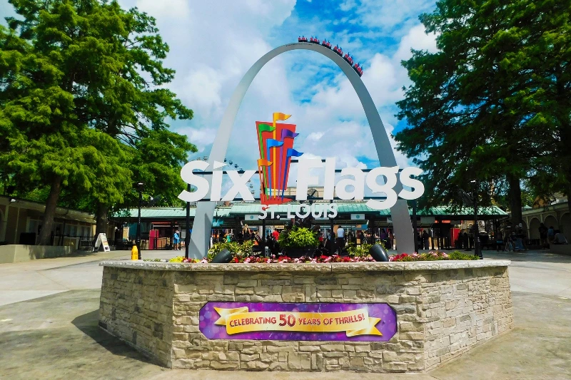 Wstęp na Six Flags St. Louis z ozdobnym łukiem i kolorowymi flagami. Na poniższym banerze jest napisane „Celebrating 50 Years of Thrills!”