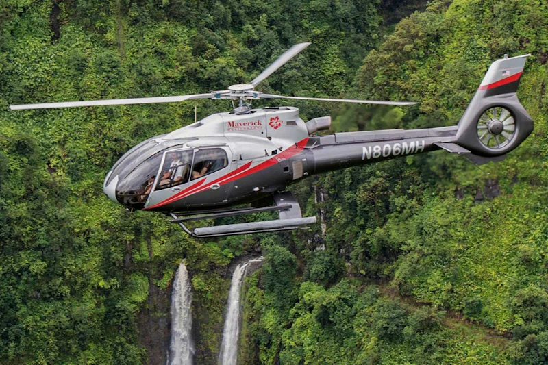 Helikopter przelatujący nad terenem zalesionym z widocznymi w tle wodospadami.
