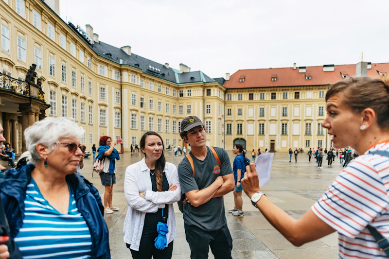 Grupa ludzi stoi na dziedzińcu otoczona zabytkowymi budynkami, jedna osoba wydaje się coś prowadzić lub wyjaśniać.