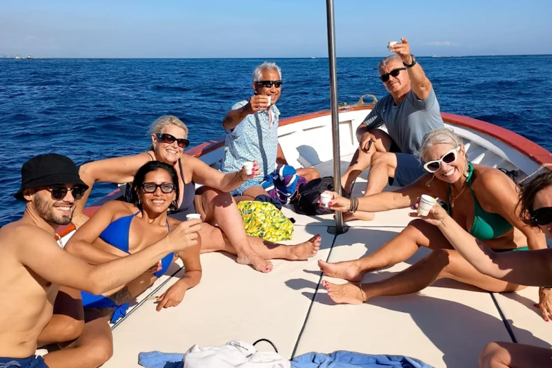 Grupa ludzi na łodzi delektująca się drinkami, z oceanem i błękitnym niebem w tle.