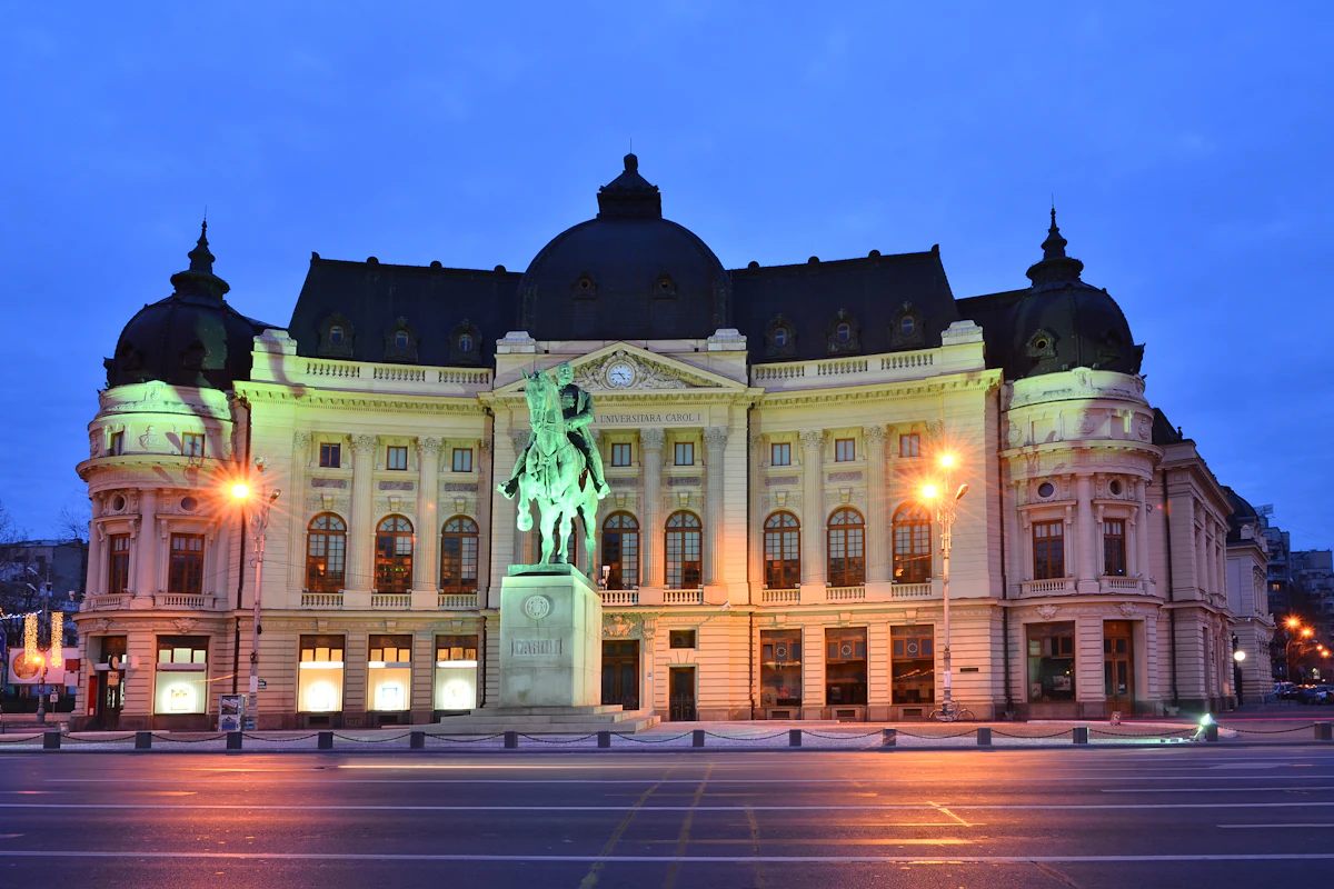 Wielki budynek z łukowatymi oknami i posągiem jeźdźca na koniu z przodu, oświetlony na tle zmierzchowego nieba.