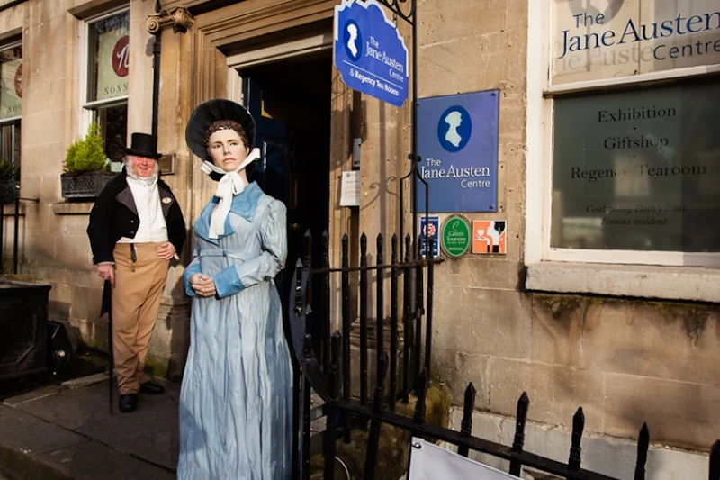 Mężczyzna w stroju z epoki stoi obok posągu kobiety przed The Jane Austen Centre.
