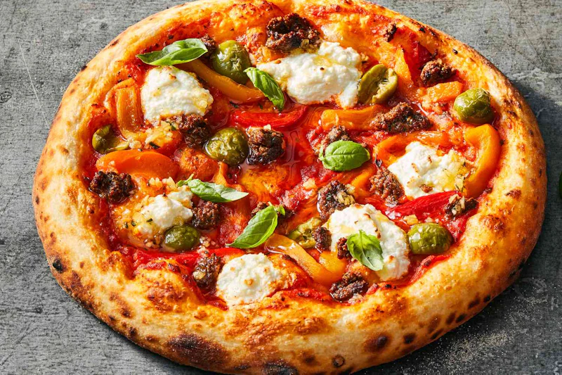 Pizza z ricottą, klopsikami, zielonymi oliwkami, liśćmi bazylii i paskami papryki na szarej powierzchni.