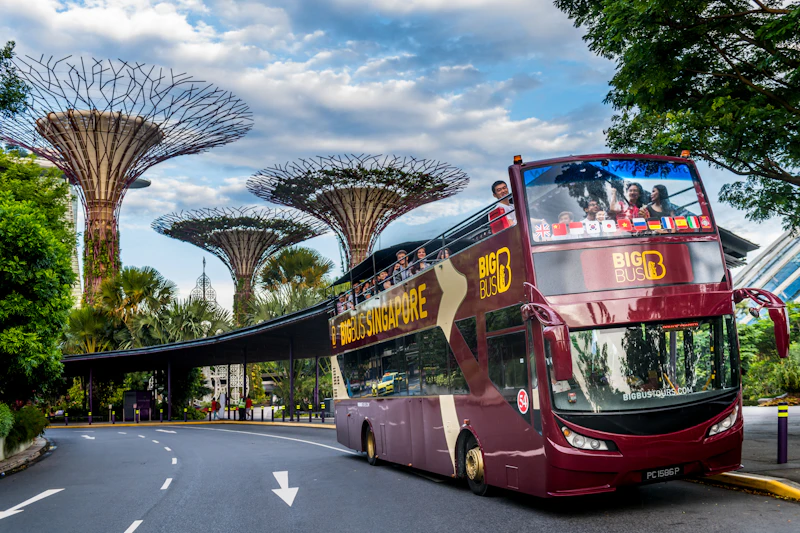 Czerwony piętrowy autobus wycieczkowy z oznakowaniem „Hippo Singapore” jedzie obok hotelu Marina Bay Sands pod częściowo zachmurzonym niebem.