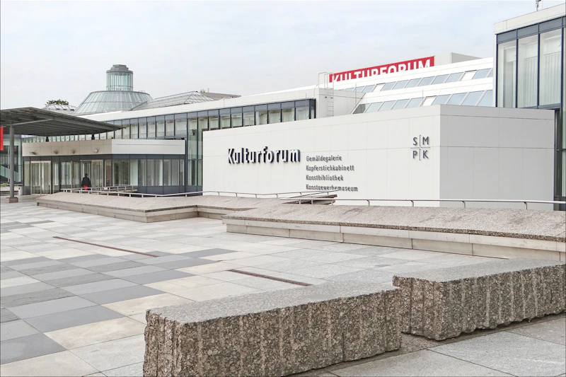 Nowoczesny kompleks budynków z dużym znakiem „Kulturforum”, szarą betonową powierzchnią zewnętrzną i ekspansywnym utwardzonym placem z przodu.