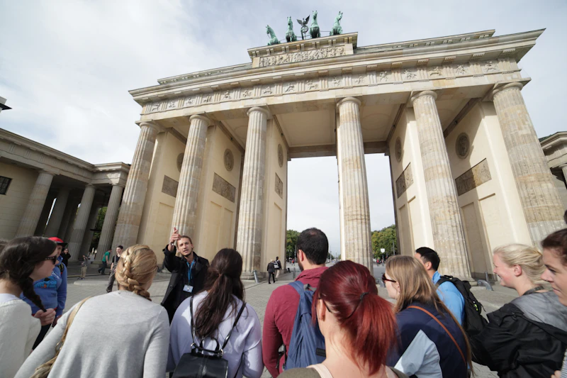 Ludzie stoją przed Bramą Brandenburską, neoklasycznym pomnikiem z kolumnami i kwadrygą na górze, w Berlinie.