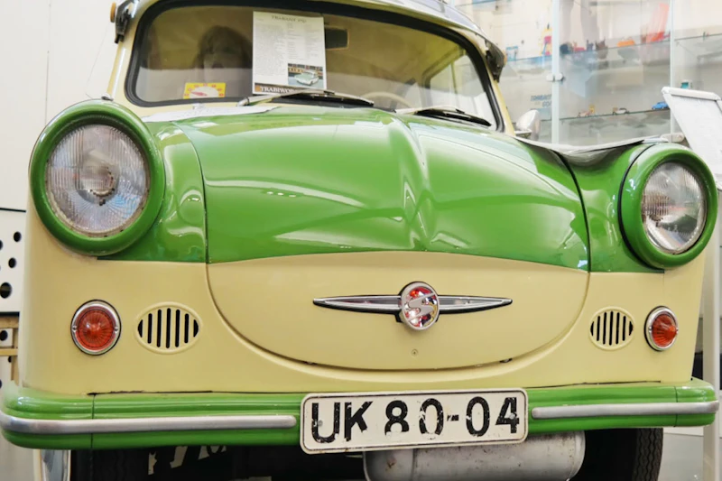 Vintage zielony i kremowy samochód wystawiony w muzeum z tablicą rejestracyjną „UK 80-04” i różnymi artefaktami w tle.