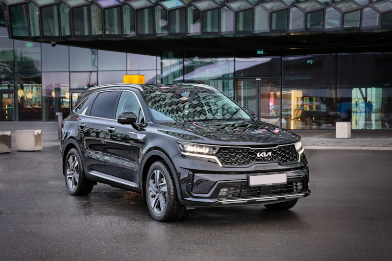 Czarny SUV zaparkowany na mokrej nawierzchni przed nowoczesnym szklanym budynkiem o geometrycznych wzorach.