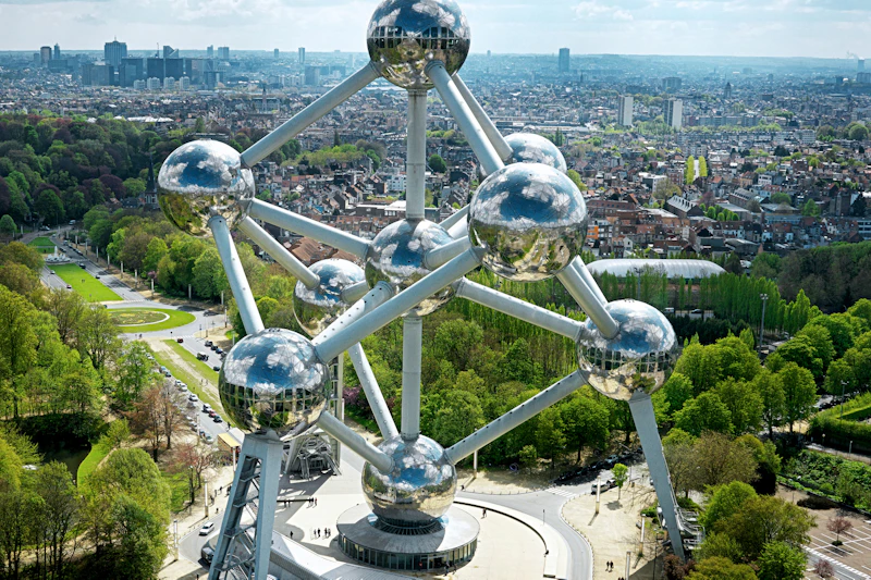 Widok z lotu ptaka na Atomium w Brukseli z odblaskowymi kulami i rurami łączącymi, w otoczeniu krajobrazu miejskiego i terenów zielonych.