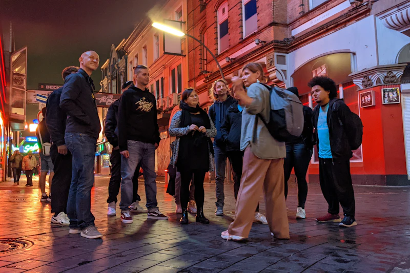 Kobieta prowadząca grupę ludzi na ulicy miejskiej w pobliżu czerwonych budynków o zmierzchu.