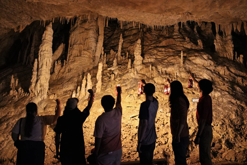 Grupa osób obserwujących stalaktyty i stalagmity wewnątrz słabo oświetlonej jaskini, oświetlonej czerwonymi latarniami.