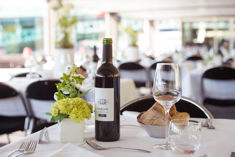 Stół jadalny z butelką wina Merlot, kieliszkiem, chlebem w misce i przyborami kuchennymi w eleganckiej restauracji.