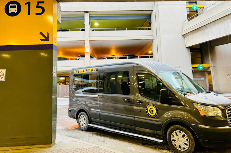 Czarna furgonetka osobowa z etykietą „The Fairy Bus” zaparkowana w wielopiętrowym garażu przy żółtym filarze z numerem 15.